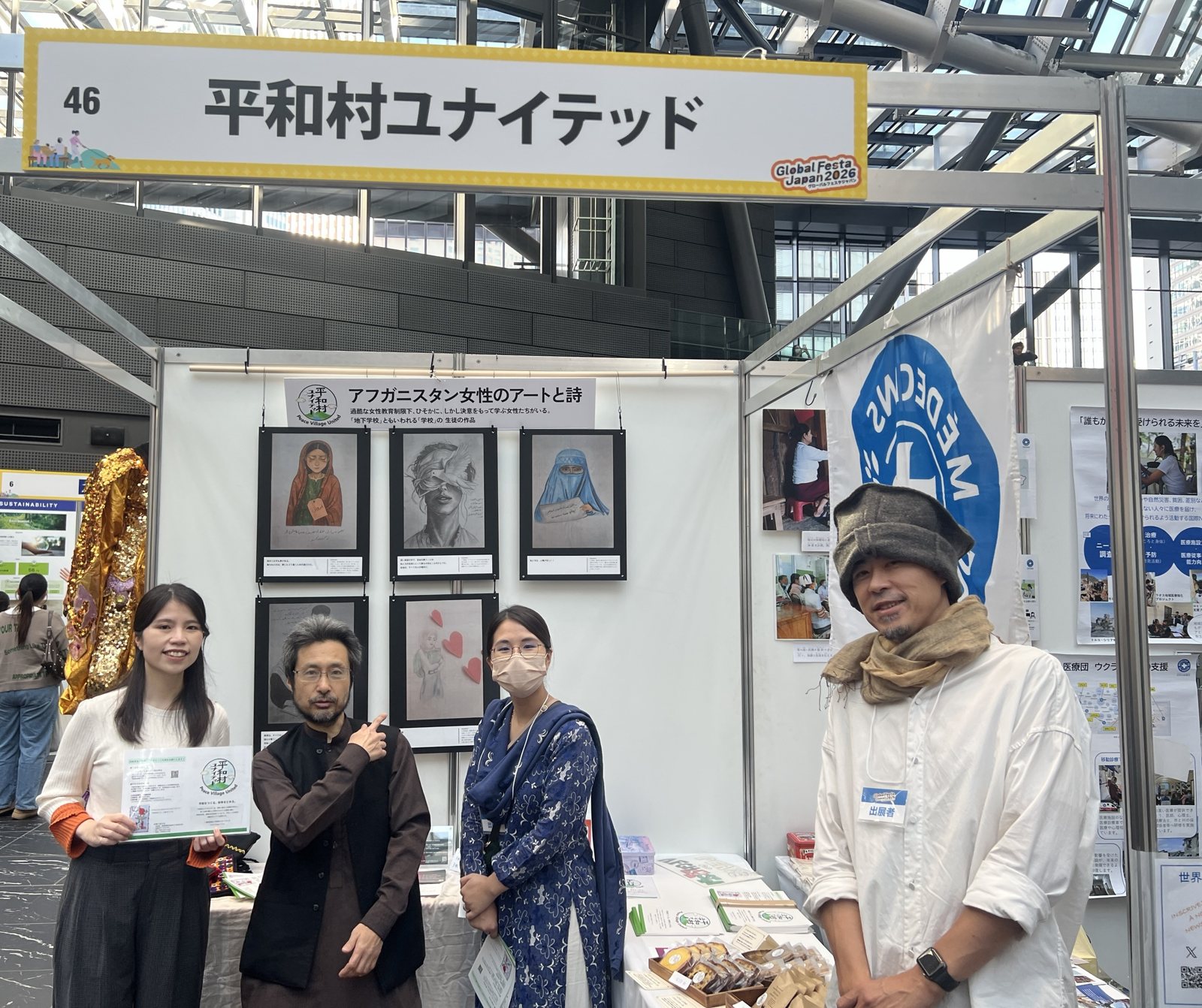 グローバルフェスタJAPAN 2026の平和村ユナイテッドのブース。アフガニスタン女性のアートと詩の展示の前に4人が並ぶ